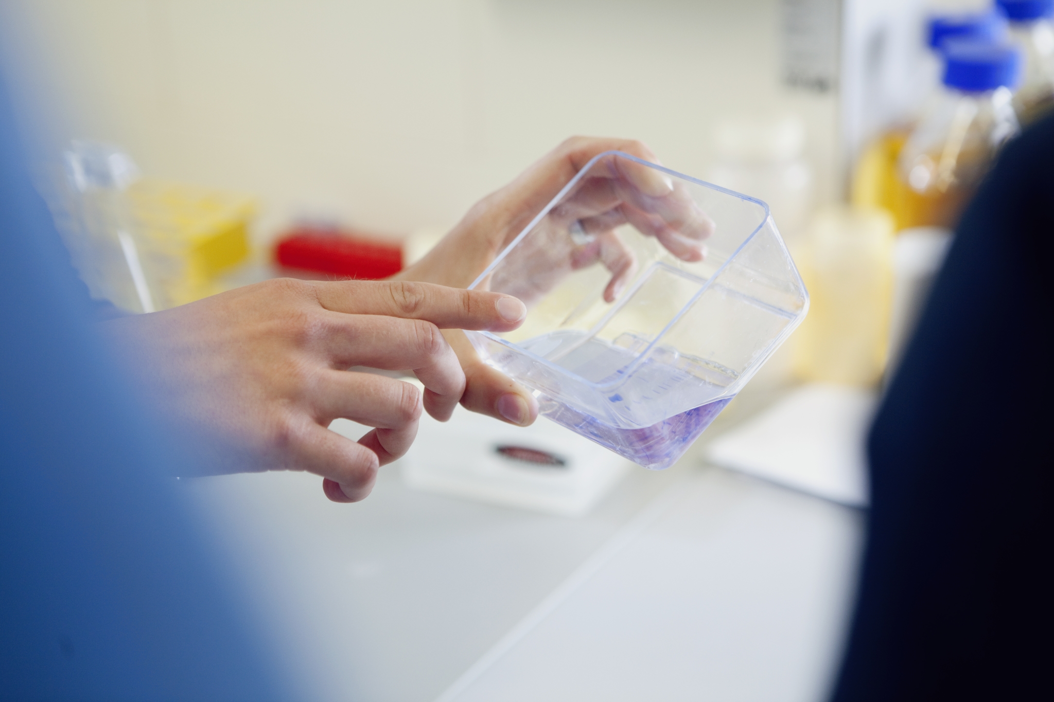 The photo shows the hands of a scientist rotating a flask with a red liquid.